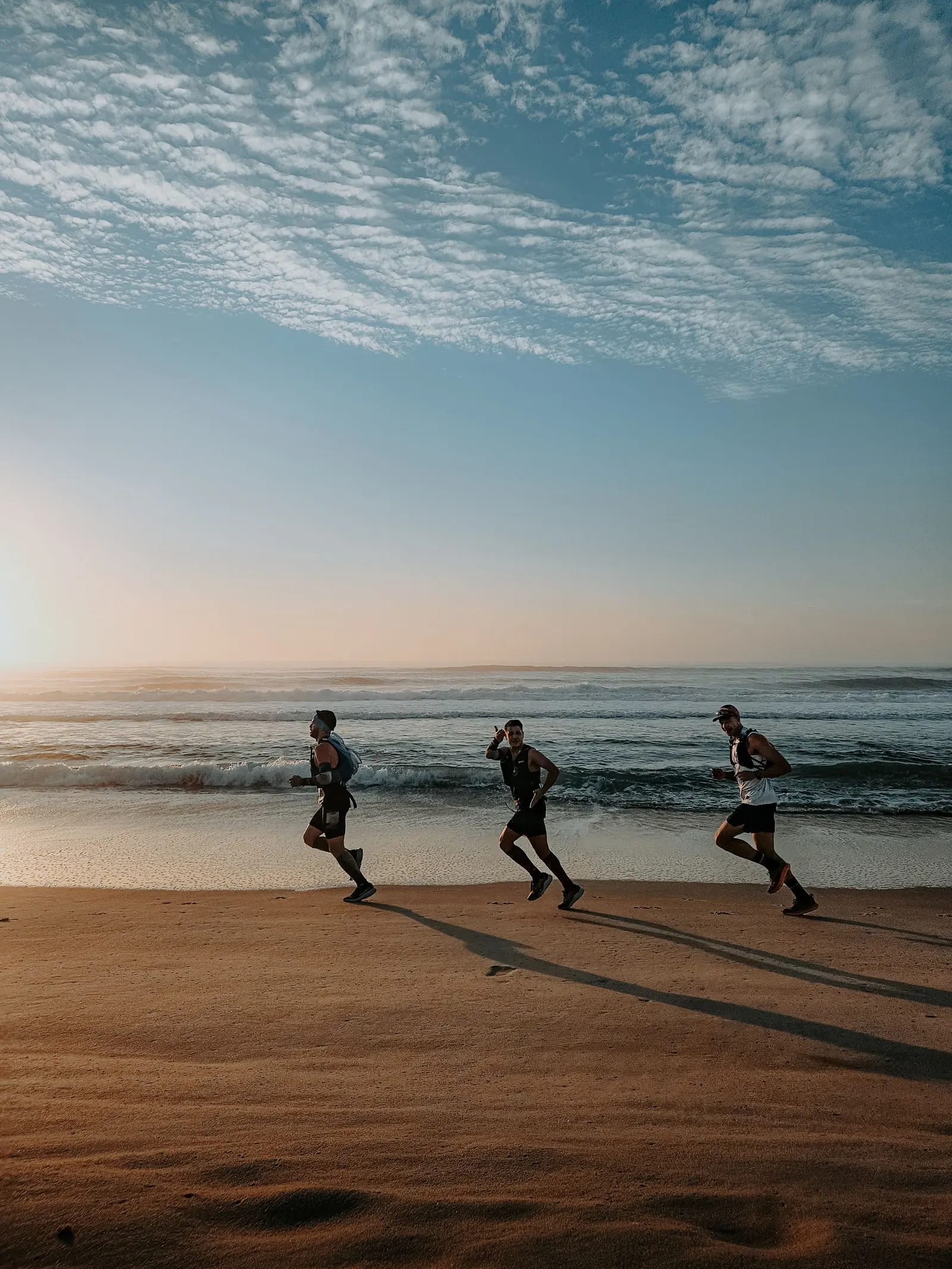 Three trail runners running together along a beach at sunrise.