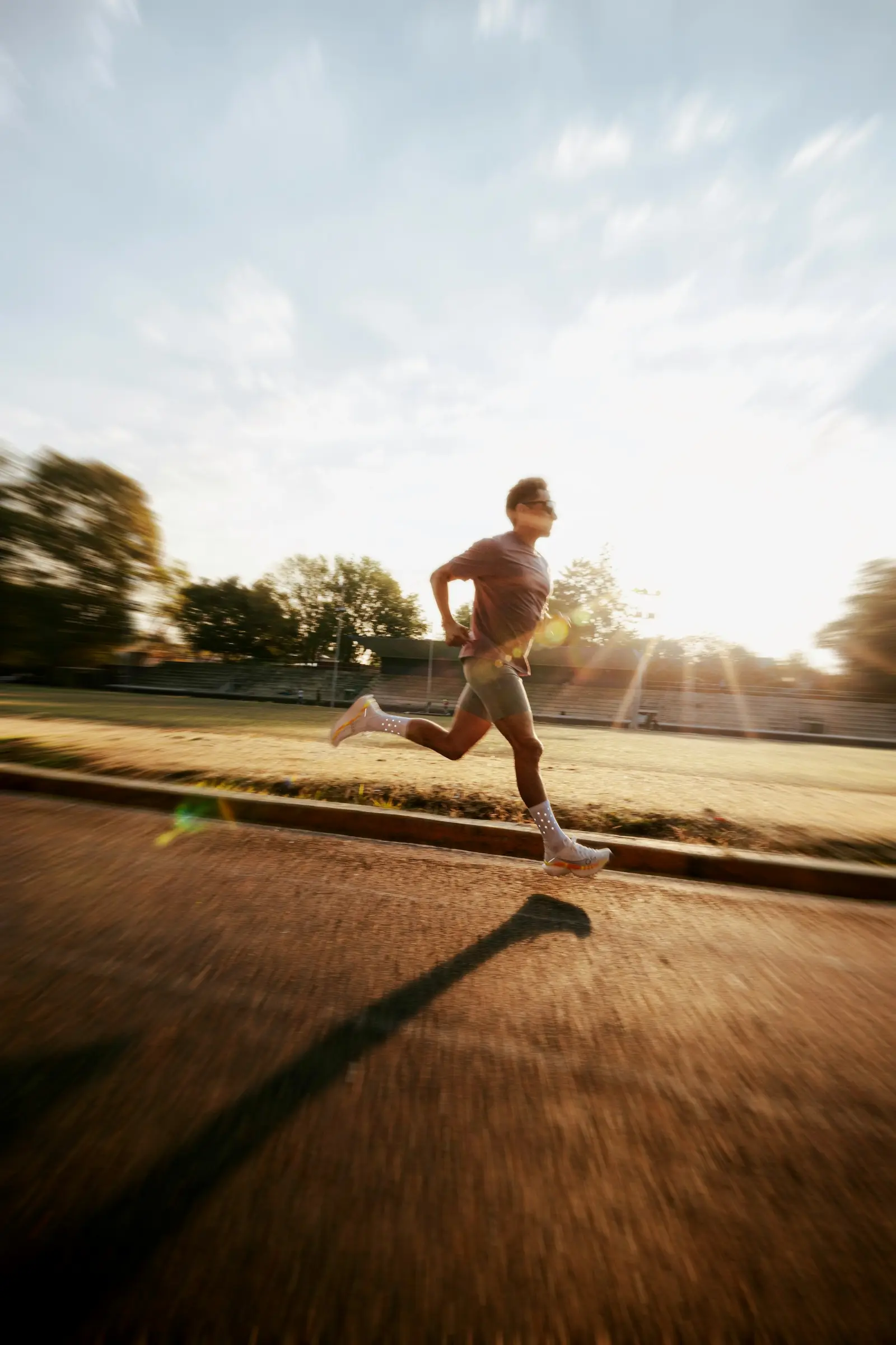 A runner in efficient form running along a sunlit outdoor track.