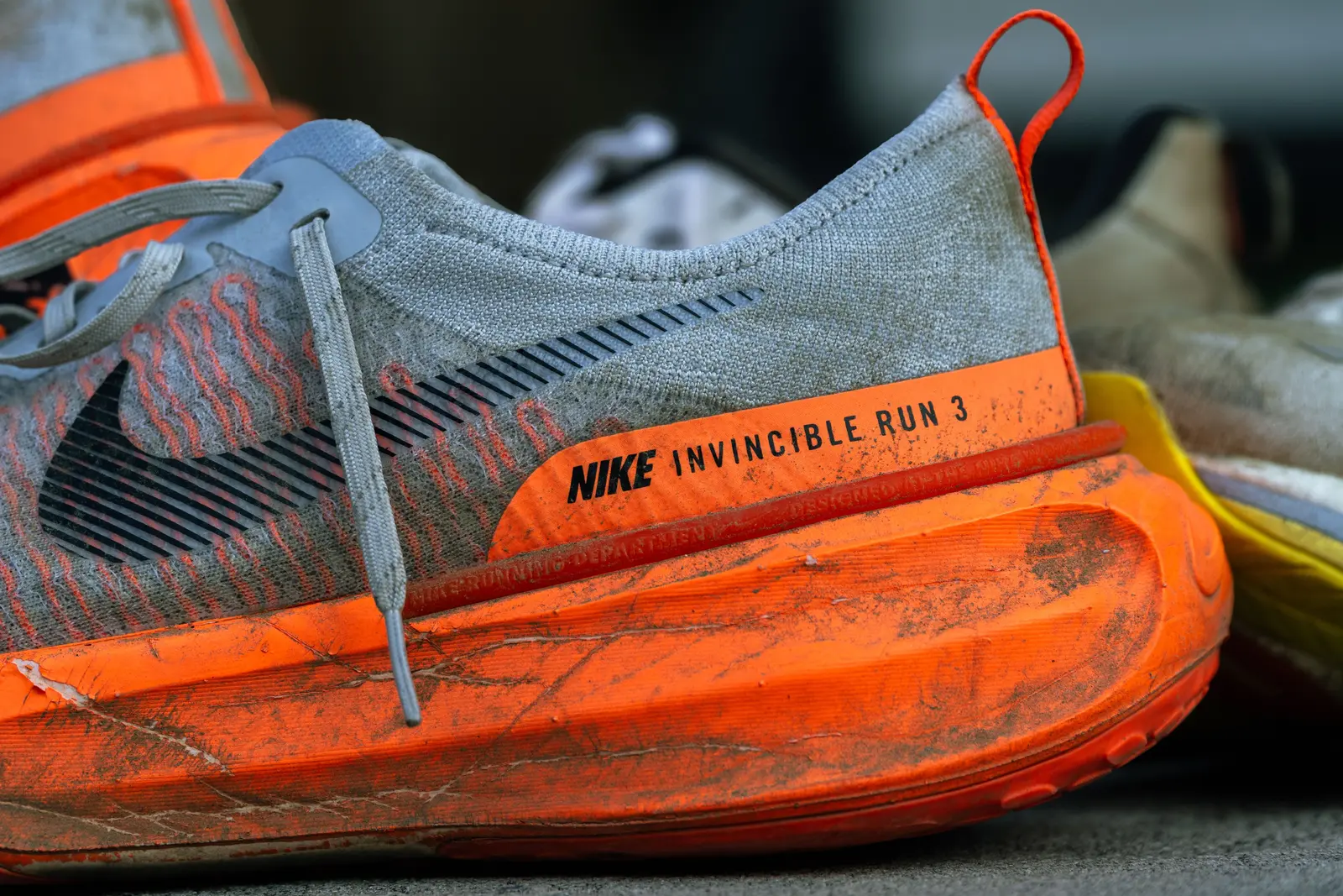 Close-up of a heavily worn, mud-splattered running shoe with a cracked, compressed orange midsole.